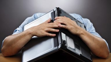 a computer is held in the arms of a man leaning back on a sofa